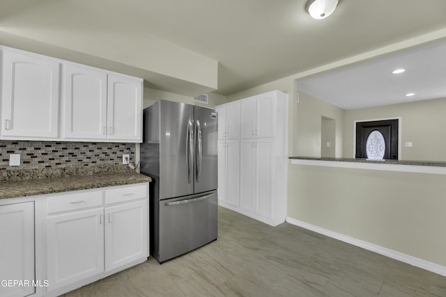 kitchen featuring tasteful backsplash, stainless steel fridge, dark stone counters, and white cabinets