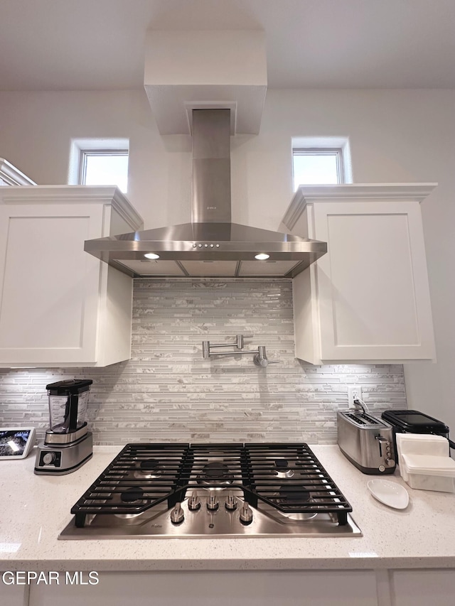 kitchen featuring wall chimney exhaust hood, white cabinetry, light stone counters, tasteful backsplash, and stainless steel gas stovetop