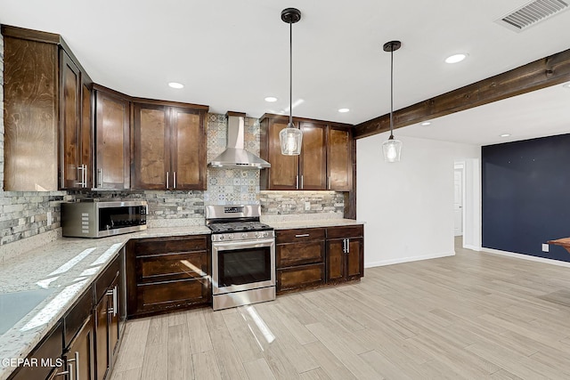 kitchen featuring appliances with stainless steel finishes, pendant lighting, beamed ceiling, light stone countertops, and wall chimney exhaust hood