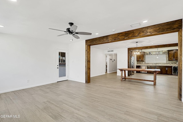 unfurnished living room featuring wine cooler, sink, ceiling fan, and light wood-type flooring