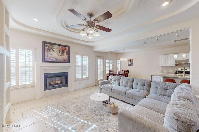 living room featuring light tile patterned flooring, track lighting, a raised ceiling, and ceiling fan