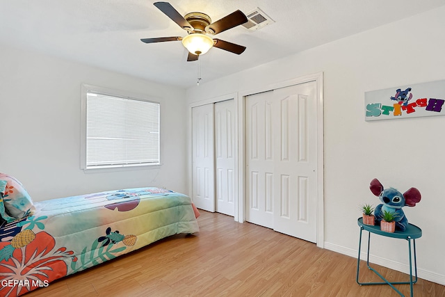 bedroom with ceiling fan, light wood-type flooring, and two closets