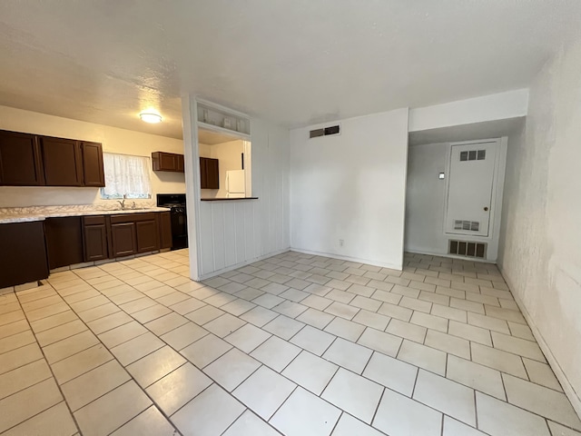 kitchen with light tile patterned flooring, sink, dark brown cabinets, and stove