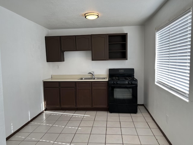 kitchen featuring black gas range oven, sink, dark brown cabinetry, and light tile patterned flooring