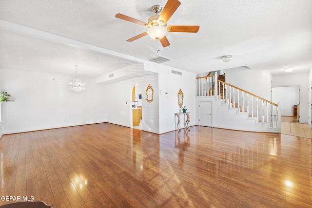 unfurnished living room featuring wood-type flooring, ceiling fan with notable chandelier, and a textured ceiling