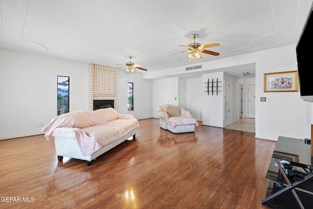 living room featuring hardwood / wood-style flooring, ceiling fan, a brick fireplace, and a textured ceiling