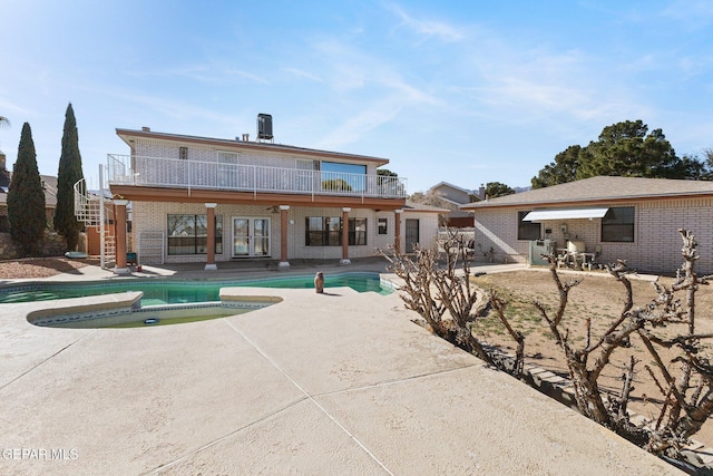 rear view of house featuring french doors, a balcony, a pool with hot tub, and a patio