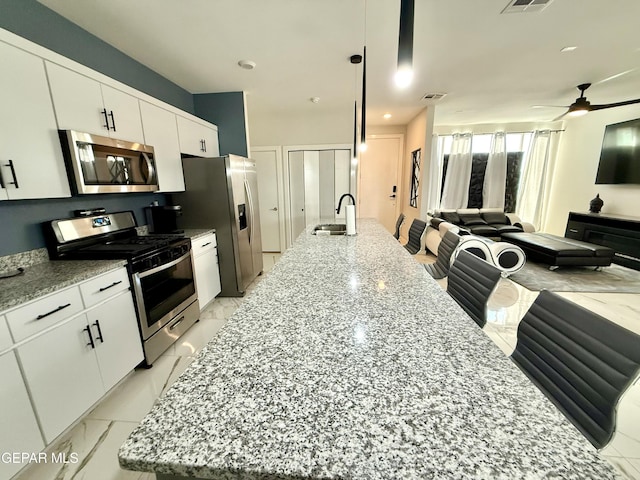 kitchen with a kitchen island with sink, decorative light fixtures, stainless steel appliances, and white cabinets