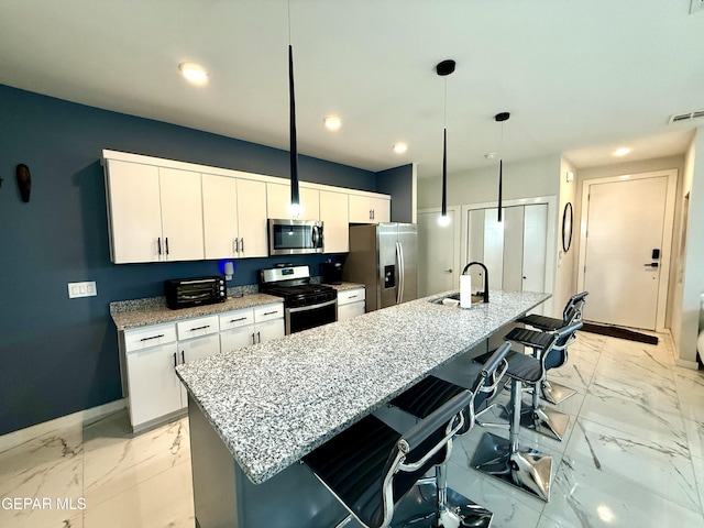 kitchen featuring appliances with stainless steel finishes, decorative light fixtures, sink, white cabinets, and a center island with sink