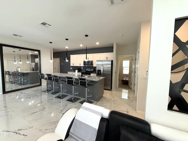 kitchen featuring white cabinetry, stainless steel appliances, decorative light fixtures, and a center island with sink