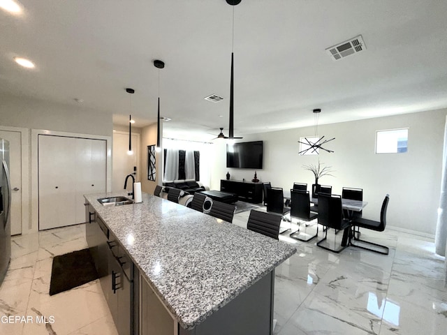 kitchen with hanging light fixtures, light stone countertops, sink, and a center island with sink