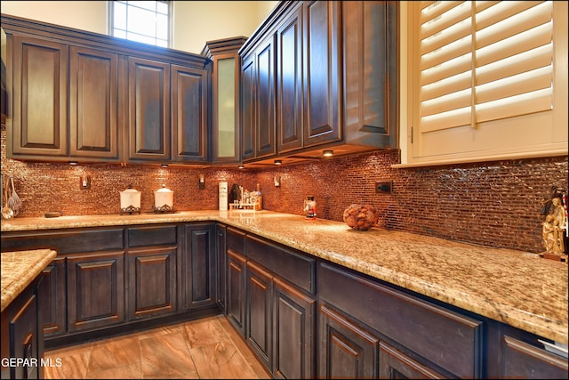 kitchen with backsplash, dark brown cabinets, and light stone countertops