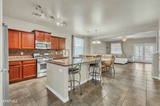 kitchen featuring decorative light fixtures, a kitchen breakfast bar, decorative backsplash, stainless steel appliances, and a center island with sink