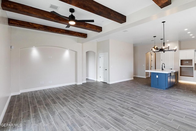 unfurnished living room featuring beamed ceiling and ceiling fan with notable chandelier