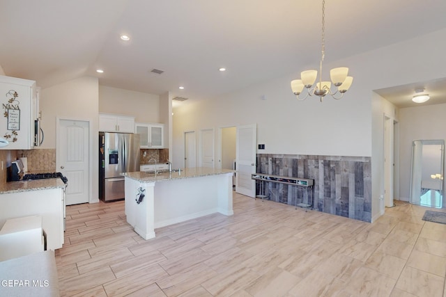 kitchen featuring appliances with stainless steel finishes, pendant lighting, white cabinetry, decorative backsplash, and a kitchen island with sink