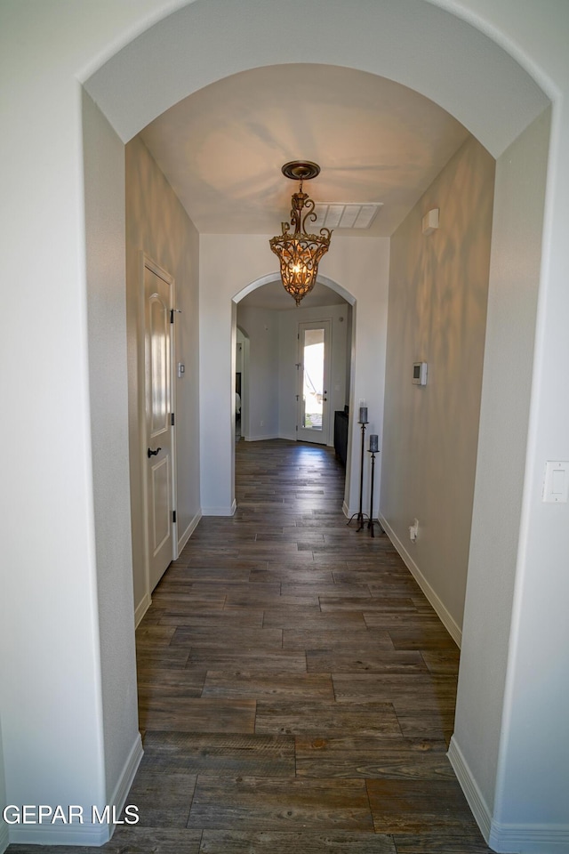 hallway featuring an inviting chandelier and dark wood-type flooring