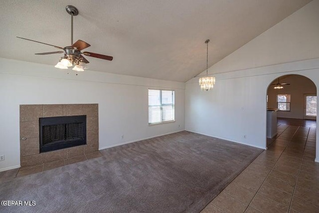 unfurnished living room featuring lofted ceiling, dark tile patterned flooring, ceiling fan with notable chandelier, and a fireplace