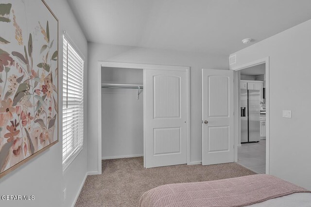 bedroom featuring stainless steel fridge, light carpet, and a closet