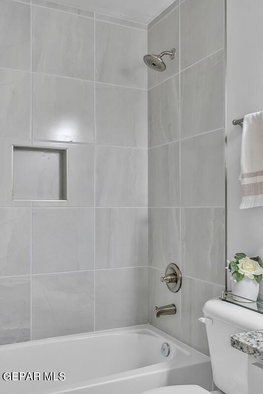 bathroom with toilet and tiled shower / bath combo