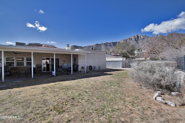 rear view of property with a mountain view, a patio area, ceiling fan, and a lawn