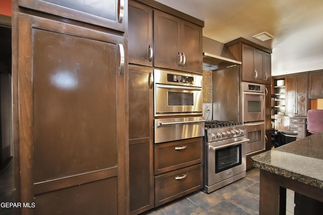 kitchen with dark stone countertops, dark brown cabinetry, and appliances with stainless steel finishes