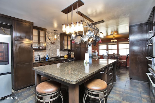 kitchen featuring a breakfast bar area, dark brown cabinets, hanging light fixtures, dark stone countertops, and a kitchen island