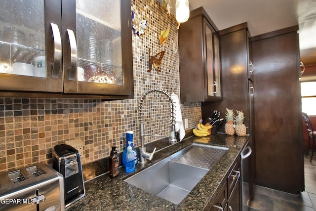 kitchen with sink, backsplash, dark brown cabinetry, and dark stone counters