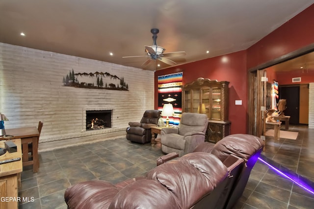 living room featuring ceiling fan, brick wall, a fireplace, and dark tile patterned flooring