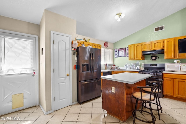 kitchen with lofted ceiling, light tile patterned floors, a breakfast bar, stainless steel appliances, and a center island