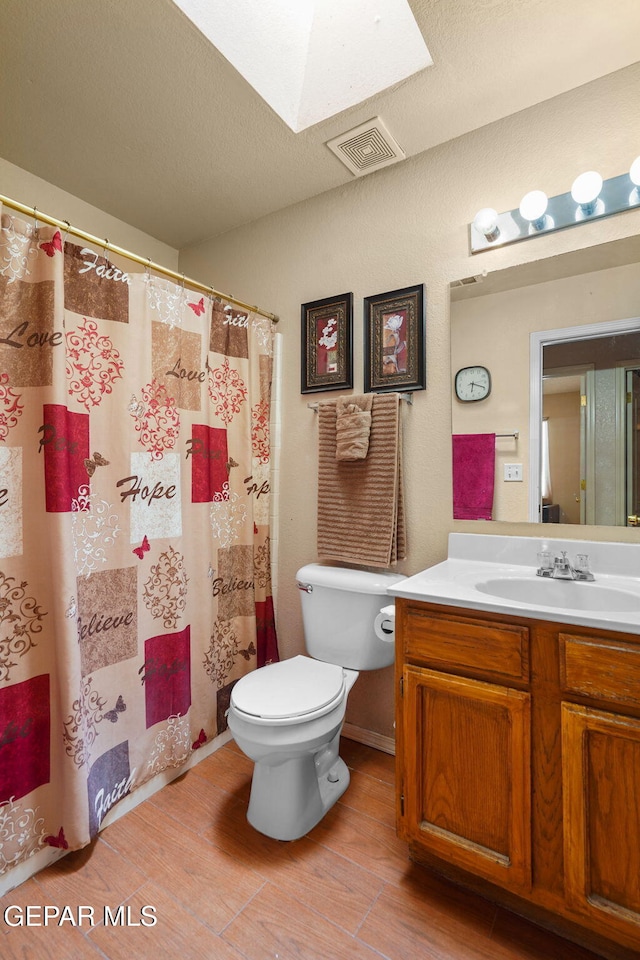 bathroom featuring hardwood / wood-style floors, a skylight, vanity, a textured ceiling, and toilet