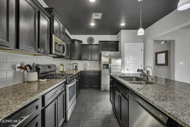 kitchen with pendant lighting, sink, stainless steel appliances, and dark stone counters