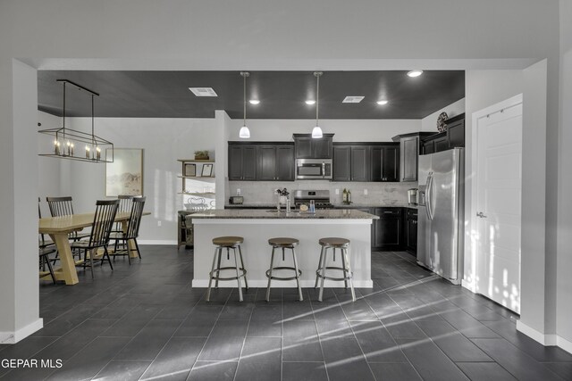 kitchen featuring appliances with stainless steel finishes, a breakfast bar, decorative light fixtures, a kitchen island with sink, and light stone countertops