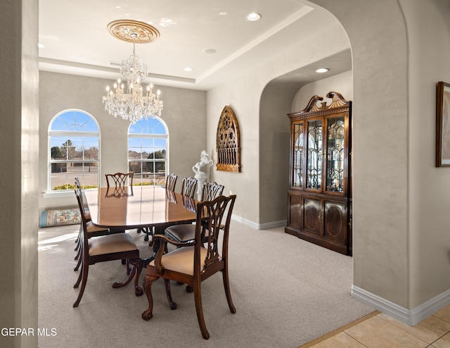 carpeted dining room with an inviting chandelier and a raised ceiling