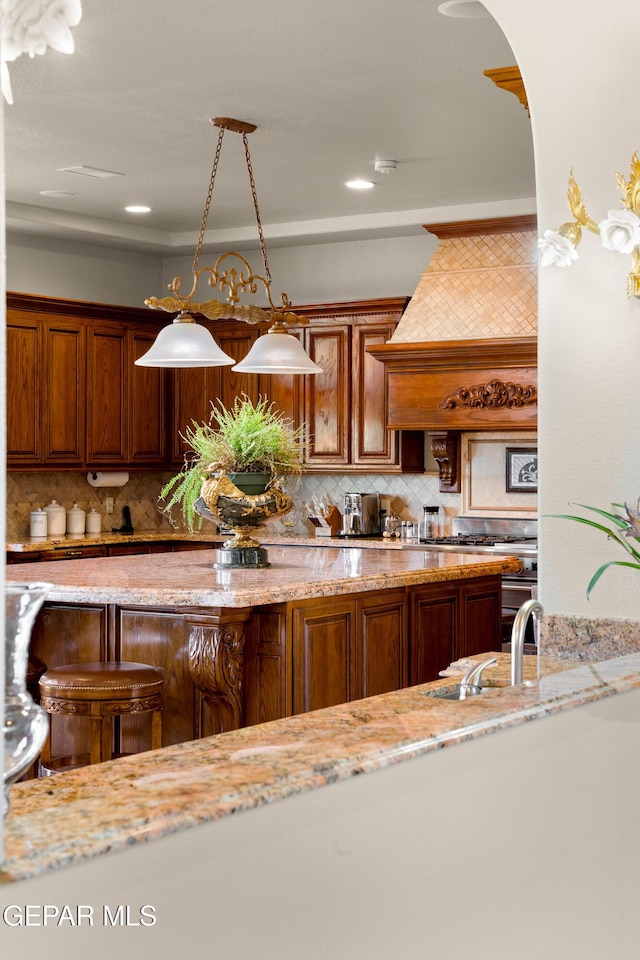 kitchen with decorative light fixtures, tasteful backsplash, sink, custom exhaust hood, and light stone countertops