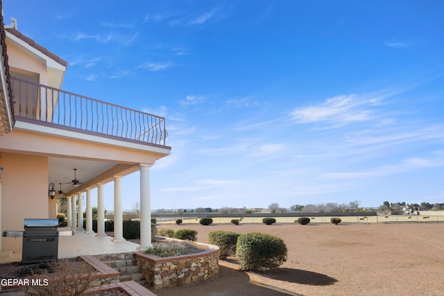 view of yard featuring a rural view, ceiling fan, a patio area, and a balcony