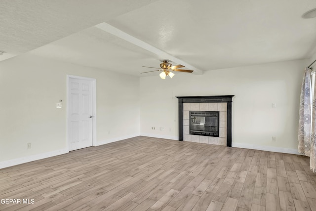 unfurnished living room featuring beam ceiling, a tile fireplace, ceiling fan, and light wood-type flooring