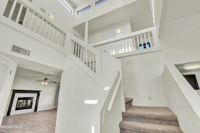 stairway featuring ceiling fan, a towering ceiling, and a fireplace