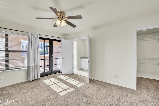 unfurnished bedroom with a walk in closet, light colored carpet, french doors, and ceiling fan