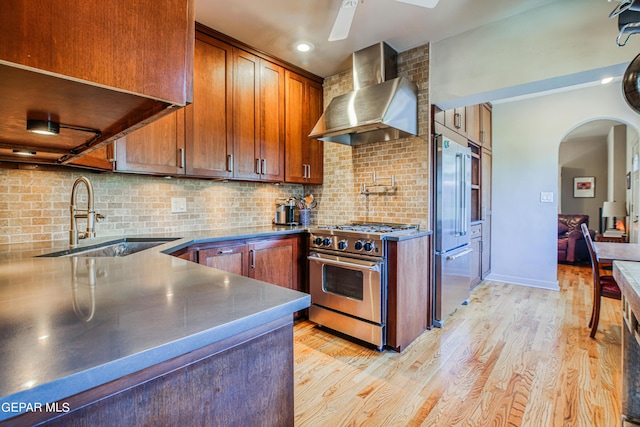 kitchen featuring wall chimney exhaust hood, sink, light hardwood / wood-style flooring, high quality appliances, and decorative backsplash