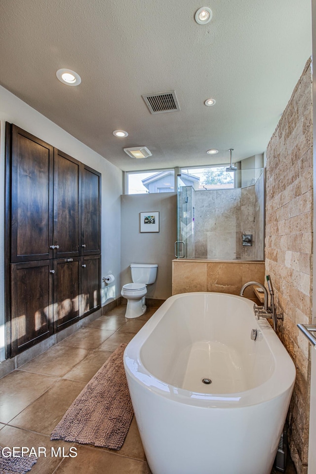 bathroom with toilet, a tile shower, a textured ceiling, and a wealth of natural light