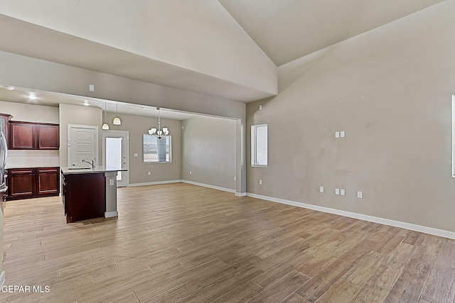 unfurnished living room featuring high vaulted ceiling, sink, a notable chandelier, and light hardwood / wood-style floors