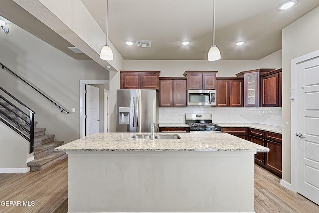 kitchen with pendant lighting, sink, appliances with stainless steel finishes, light stone counters, and a center island with sink