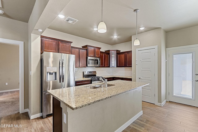 kitchen featuring sink, light stone counters, pendant lighting, stainless steel appliances, and a kitchen island with sink