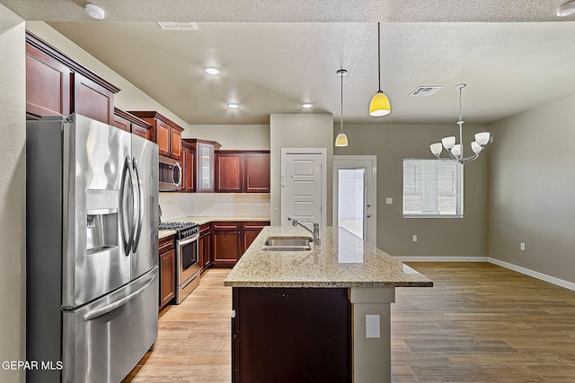 kitchen with sink, decorative light fixtures, light wood-type flooring, appliances with stainless steel finishes, and an island with sink