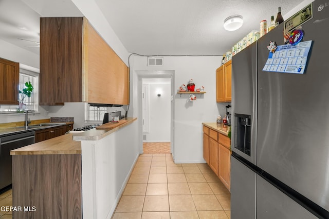 kitchen with light tile patterned flooring, sink, stainless steel fridge with ice dispenser, a textured ceiling, and black dishwasher