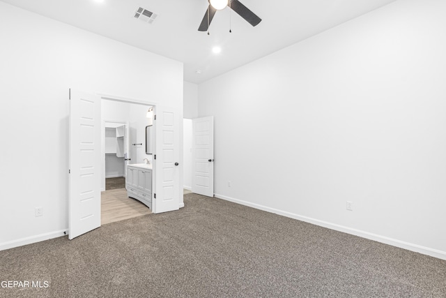 unfurnished bedroom featuring a walk in closet, light carpet, and ceiling fan