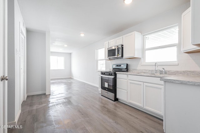 kitchen featuring stainless steel appliances, a sink, light countertops, decorative backsplash, and light wood finished floors