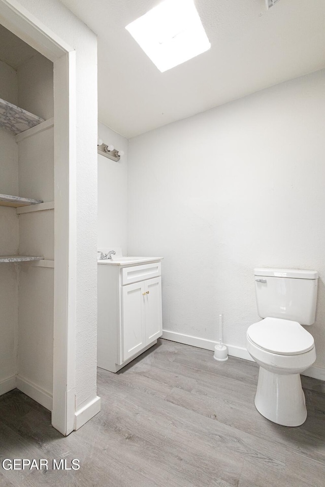 half bath with toilet, baseboards, wood finished floors, and vanity