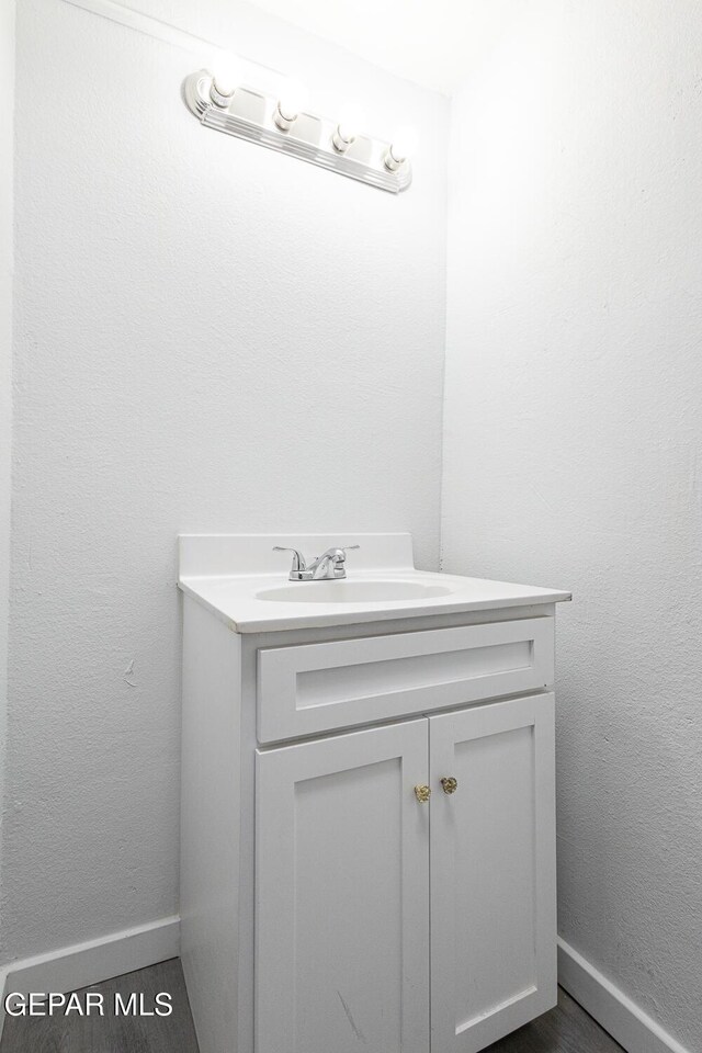 bathroom with a textured wall, baseboards, wood finished floors, and vanity