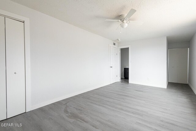 unfurnished bedroom with a closet, a textured ceiling, baseboards, and wood finished floors